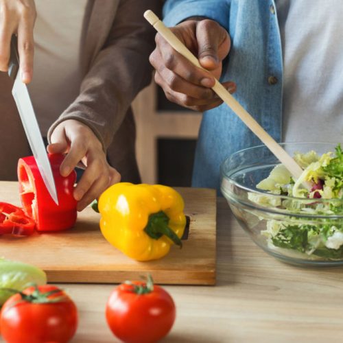Black couple preparing healthy vegetable salad together in kitchen, closeup